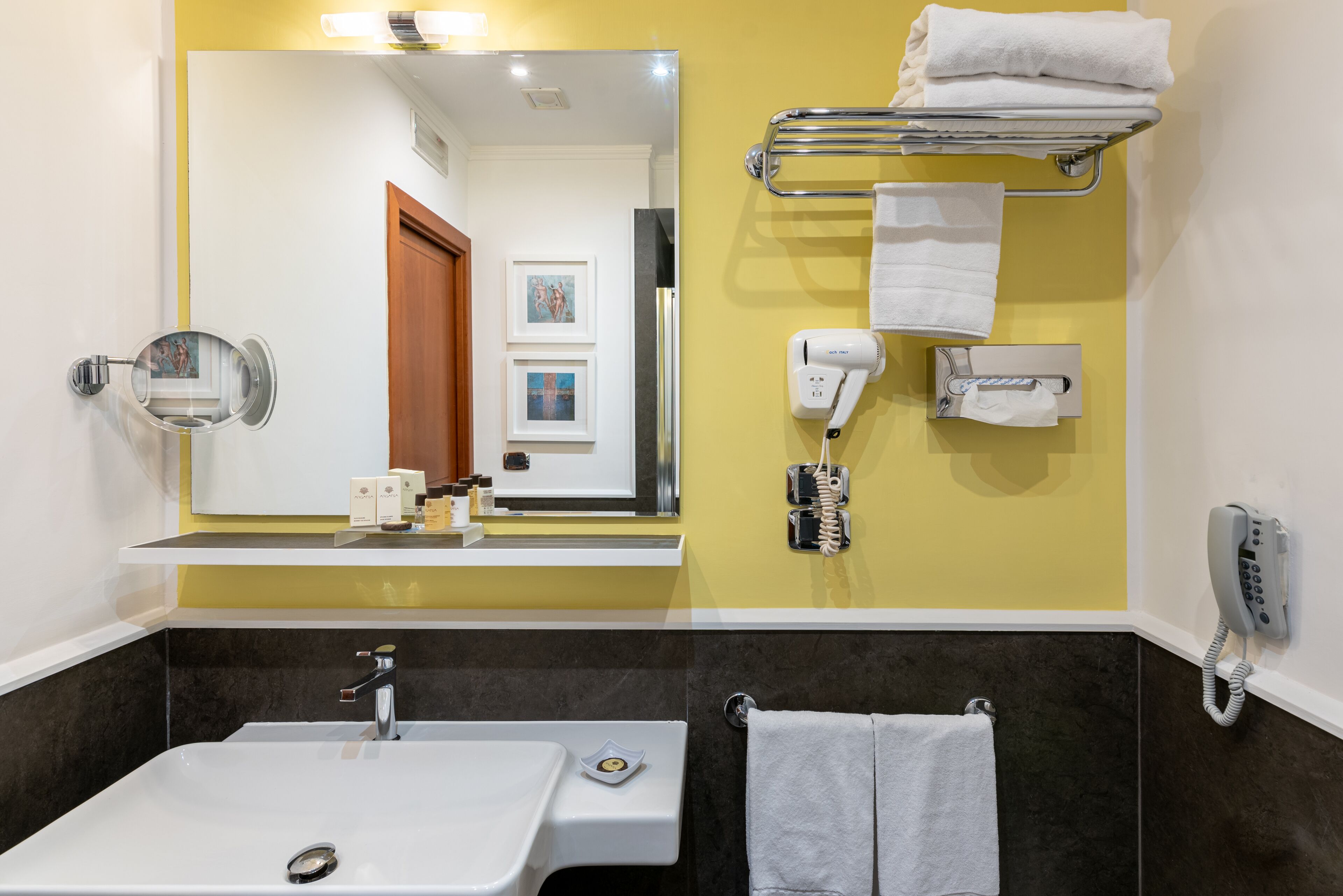 Une salle de bain avec un lavabo blanc, un miroir, un porte-serviettes avec des serviettes, un sèche-cheveux et un téléphone.