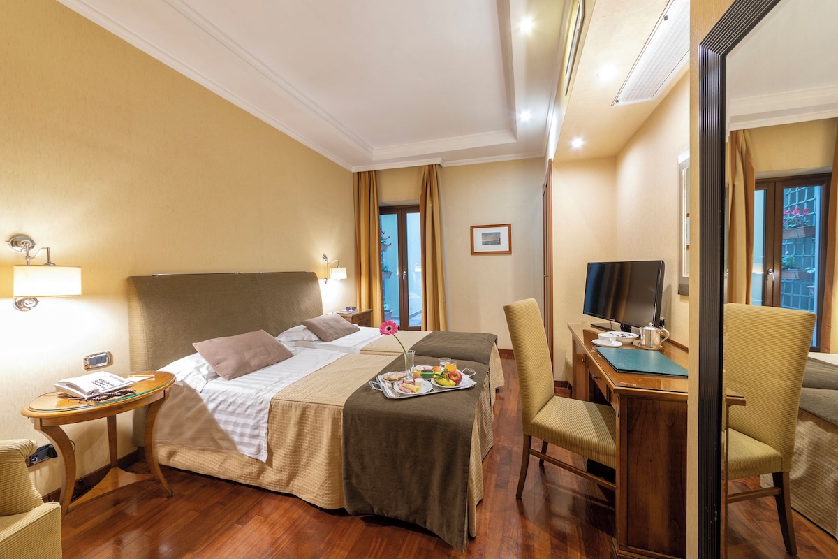 Ein Hotelzimmer mit Bett, Nachttischen, einem Schreibtisch, einem Sessel und einem Fernseher.