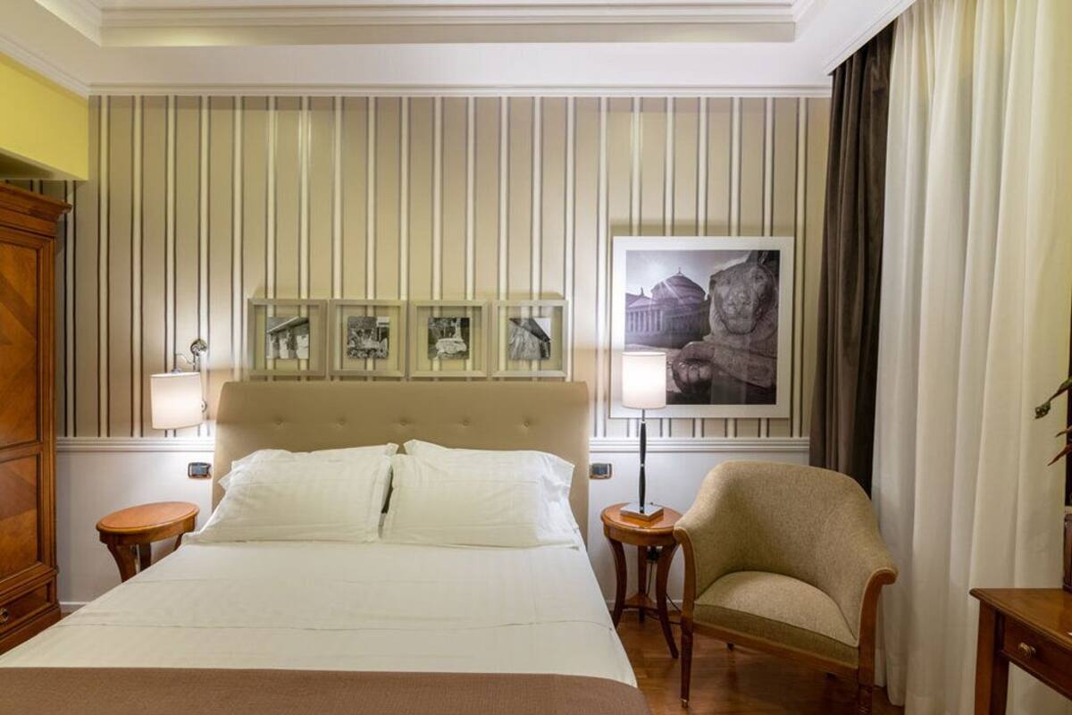 A hotel room with a large bed, a headboard with framed pictures, a chair, and a lamp.