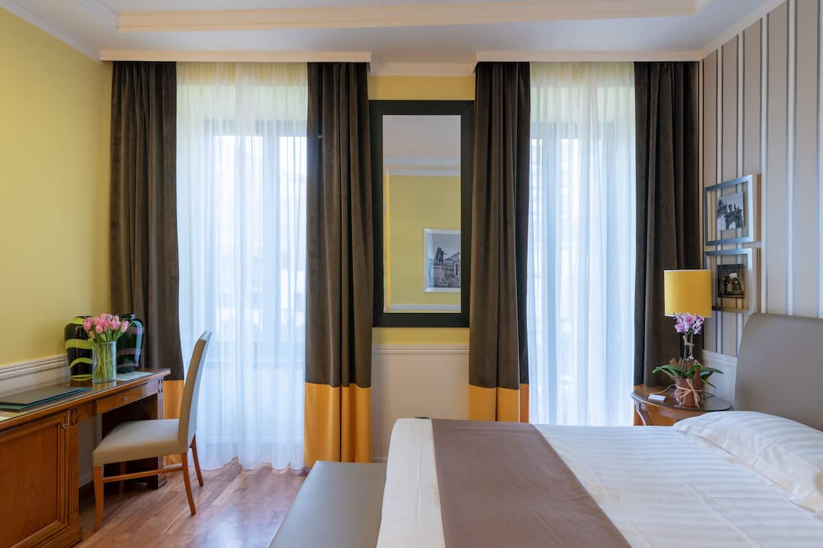 A hotel room with a bed, a desk, a chair, a nightstand, and a mirror.