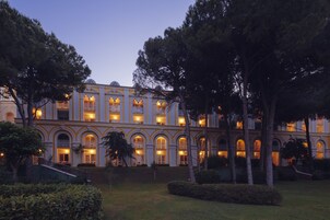 Un edificio grande de varios pisos con fachada simétrica, ventanas arqueadas y una escalera central.