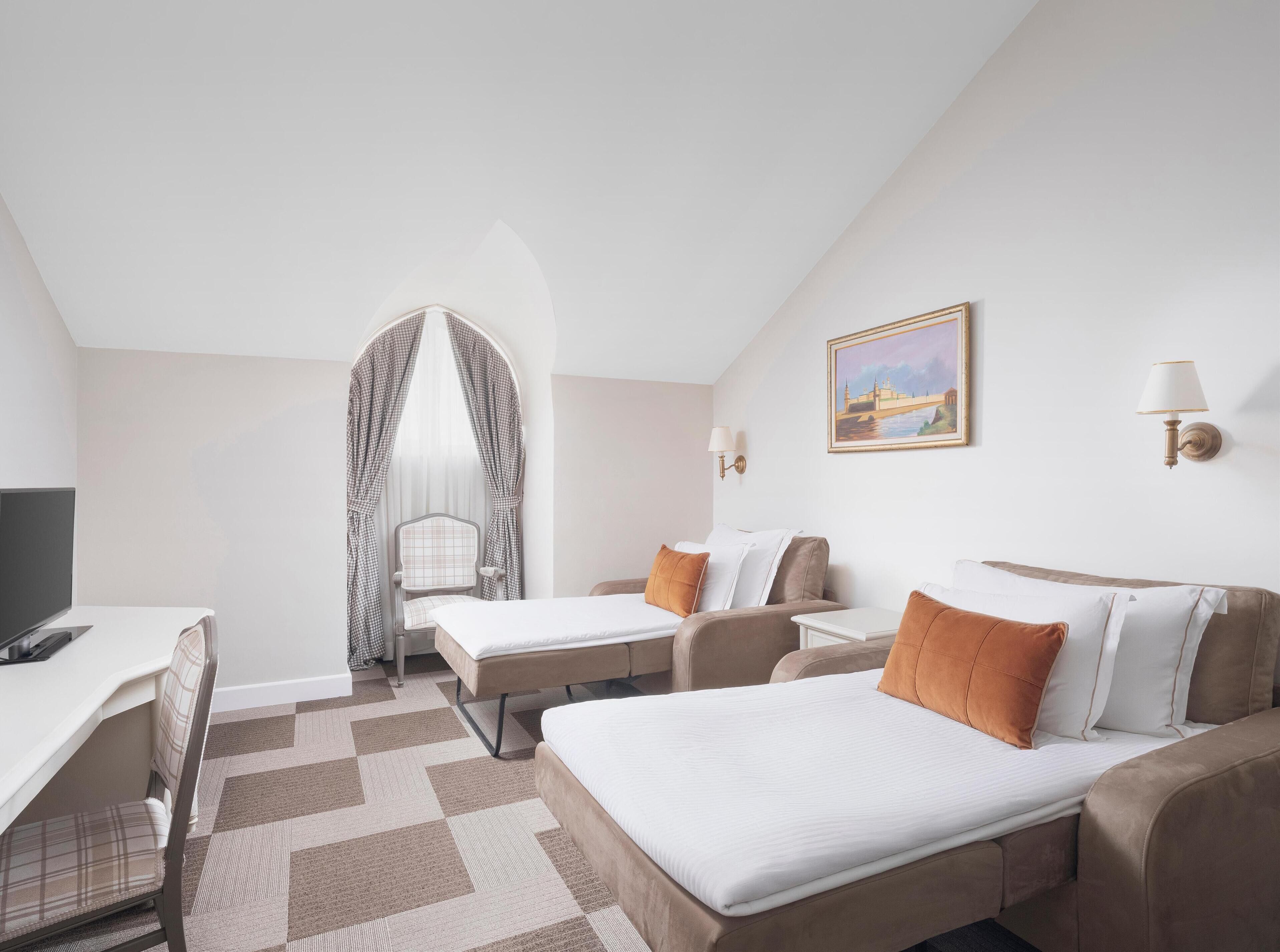 Habitación de hotel con dos camas, un escritorio y una silla. Hay un cuadro en la pared y una lámpara al lado.