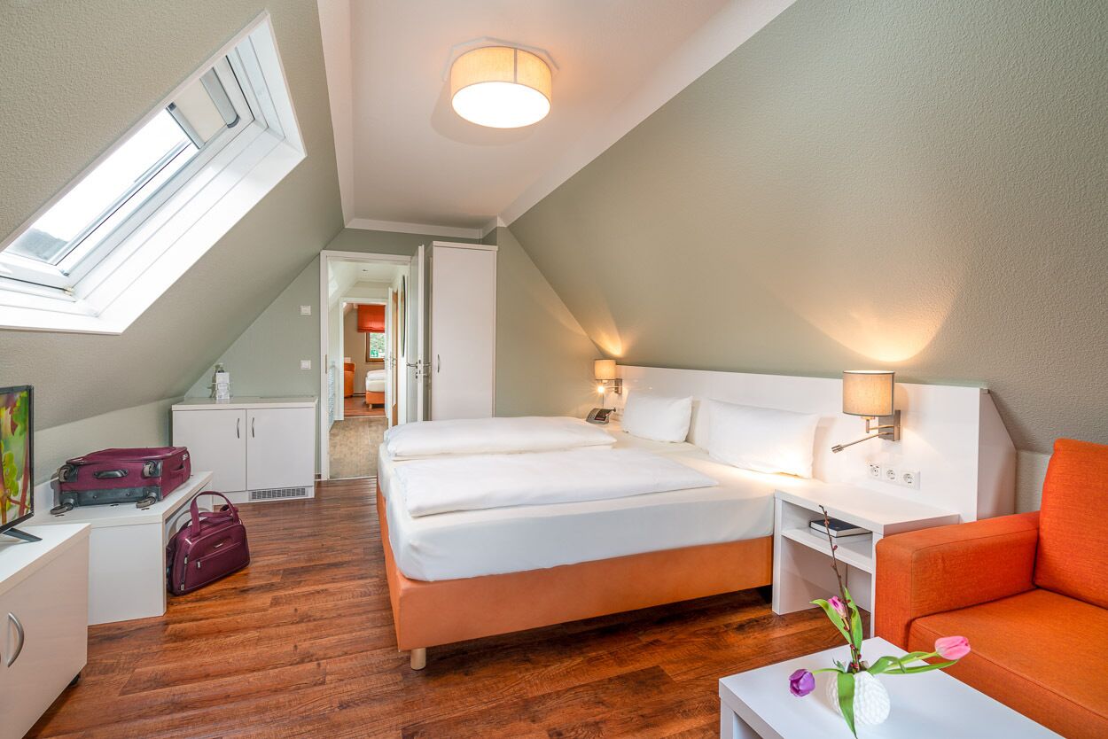 A bedroom with a bed, a desk, a chair, a lamp, a window, and a view of a hallway.