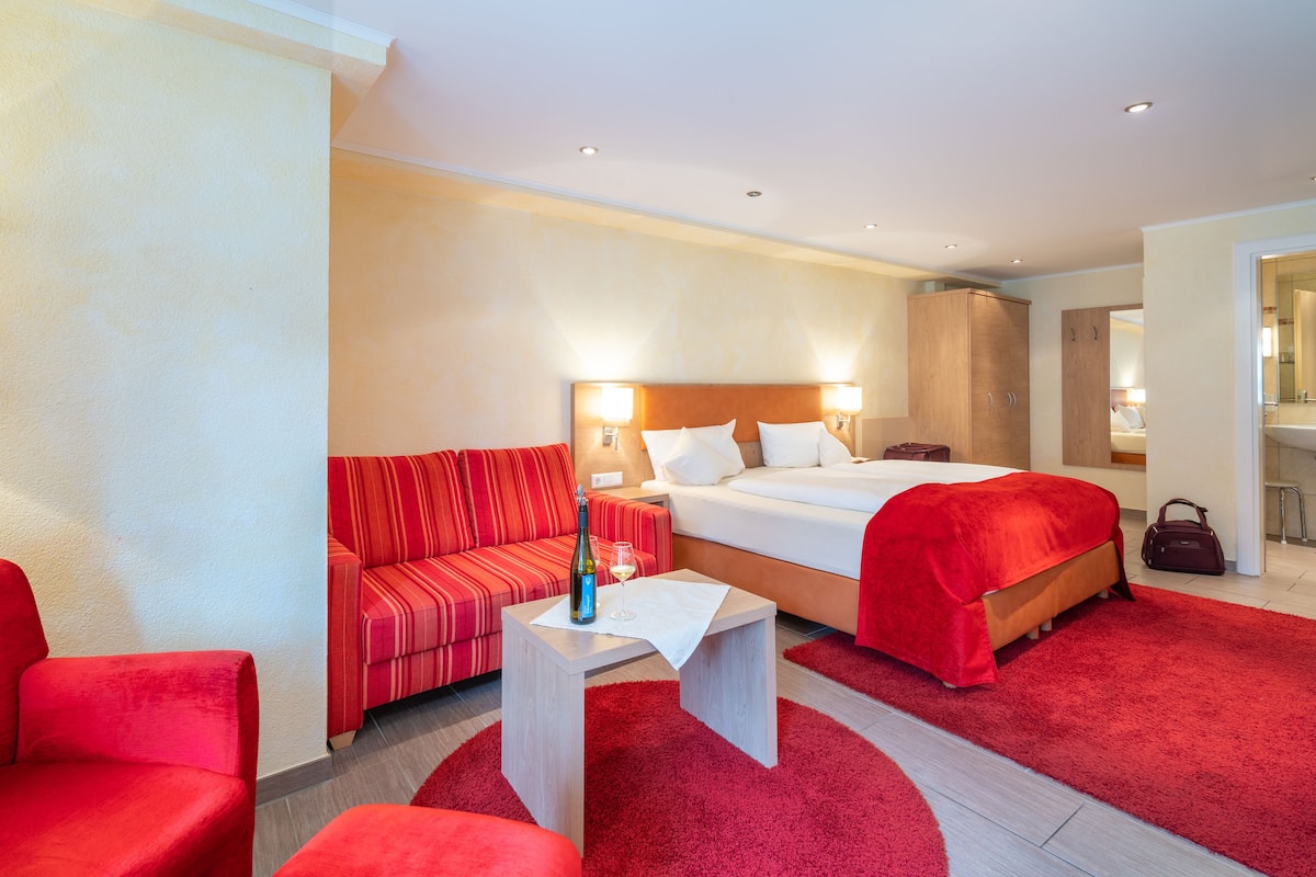 A hotel room with a bed, a sofa, a table, and a red carpet.