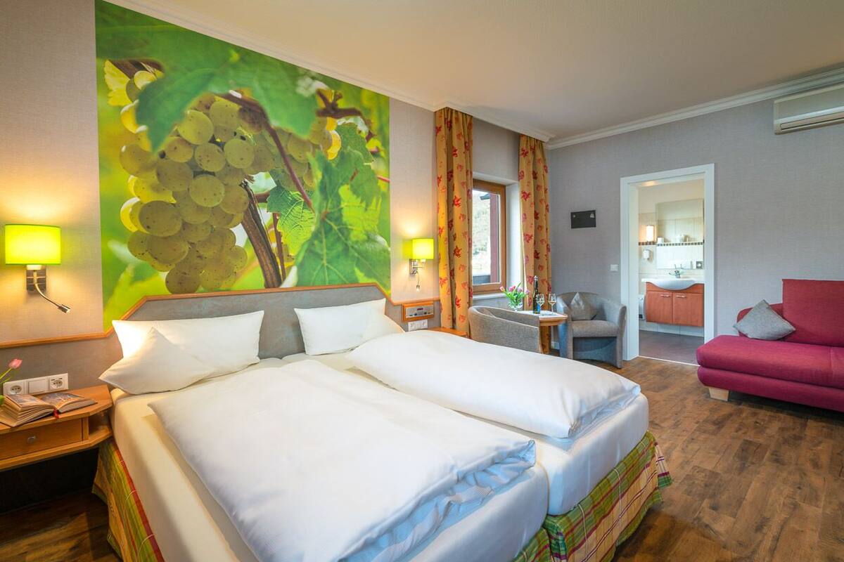 A hotel room with a large bed, two bedside tables, a chair, a small table with a plant, and a red sofa.