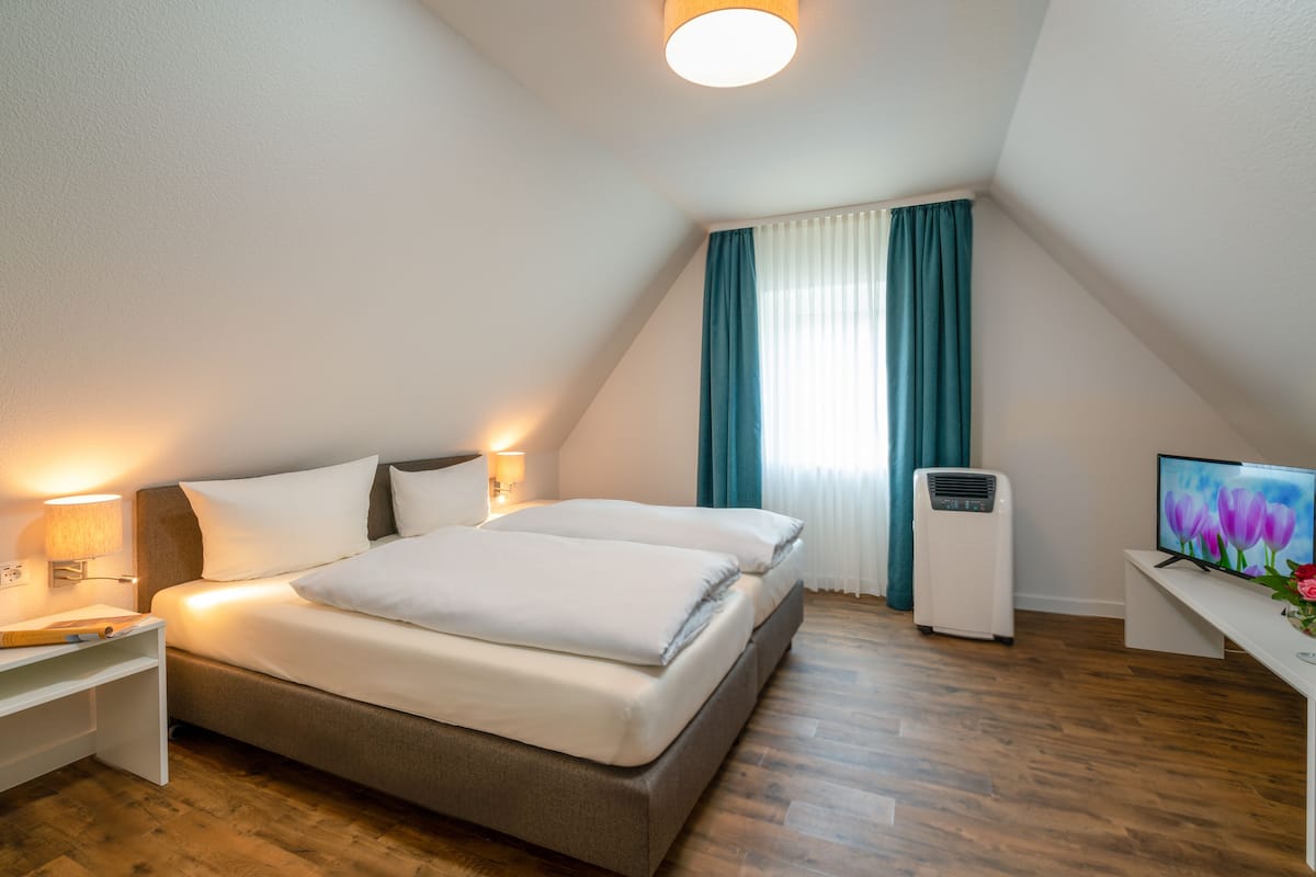 A modern bedroom with a bed, bedside table, lamp, air conditioner, and a TV on a desk.