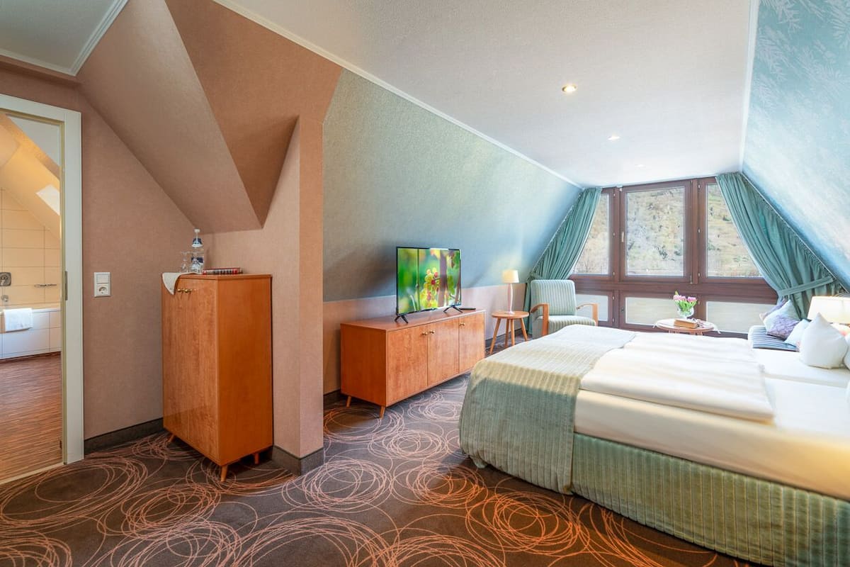 A hotel room with a bed, a desk with a TV, a cabinet, and a window with curtains.