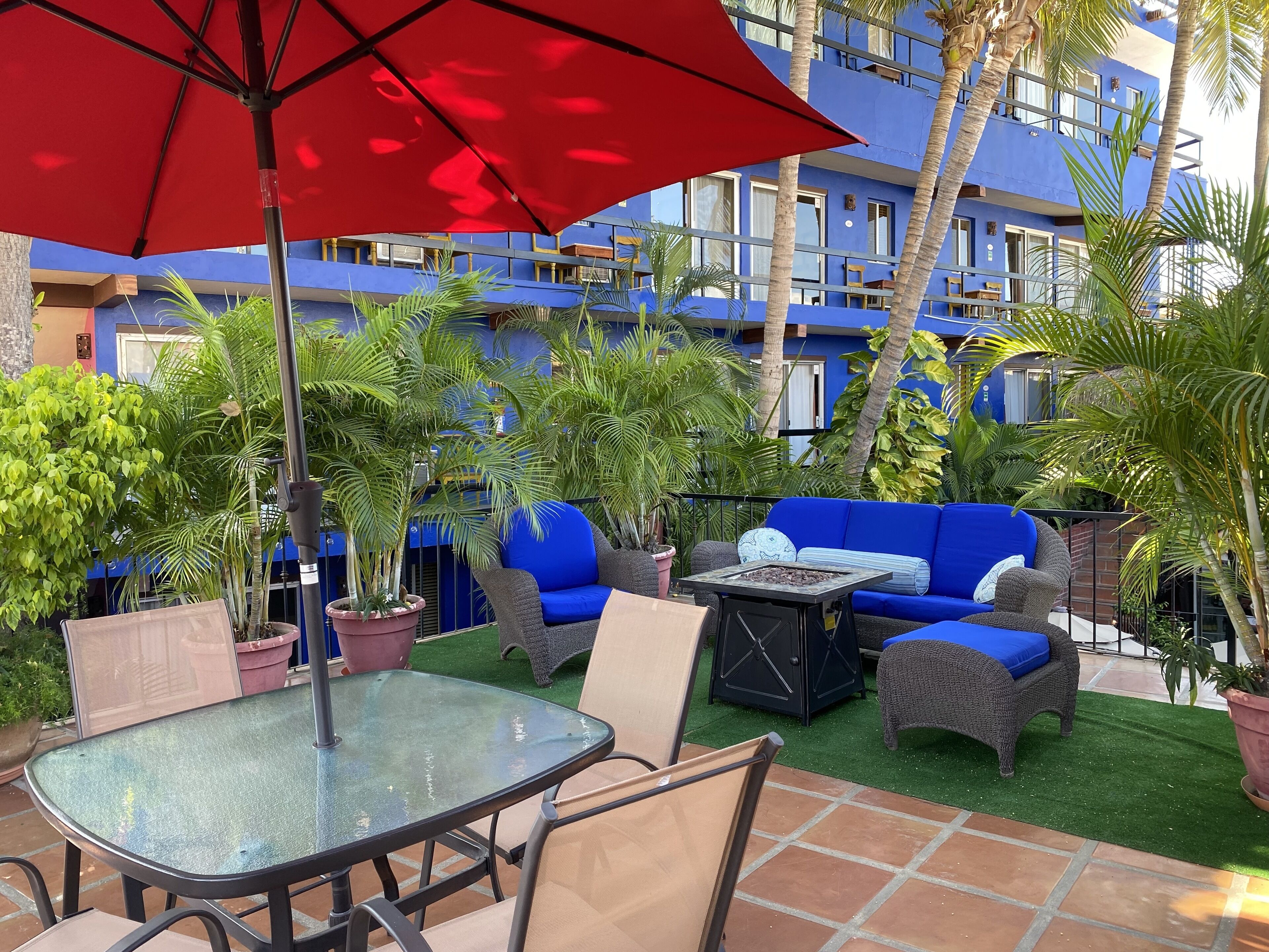 Ein Patio im Freien mit einem Glastisch, Stühlen, einem roten Sonnenschirm und einem blauen Sofa.
