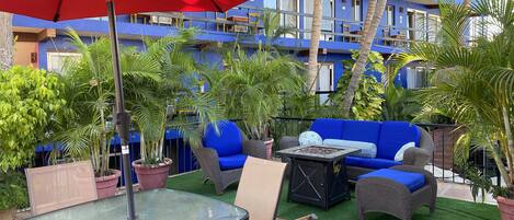 Ein Patio im Freien mit einem Glastisch, Stühlen, einem roten Sonnenschirm und einem blauen Sofa.