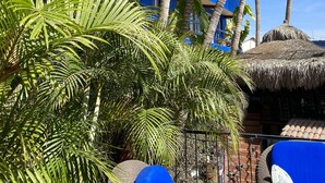 A multi-story hotel with blue and white exterior walls, palm trees, and a thatched-roof structure. - Siesta Suites Boutique Hotel (Cabo San Lucas)