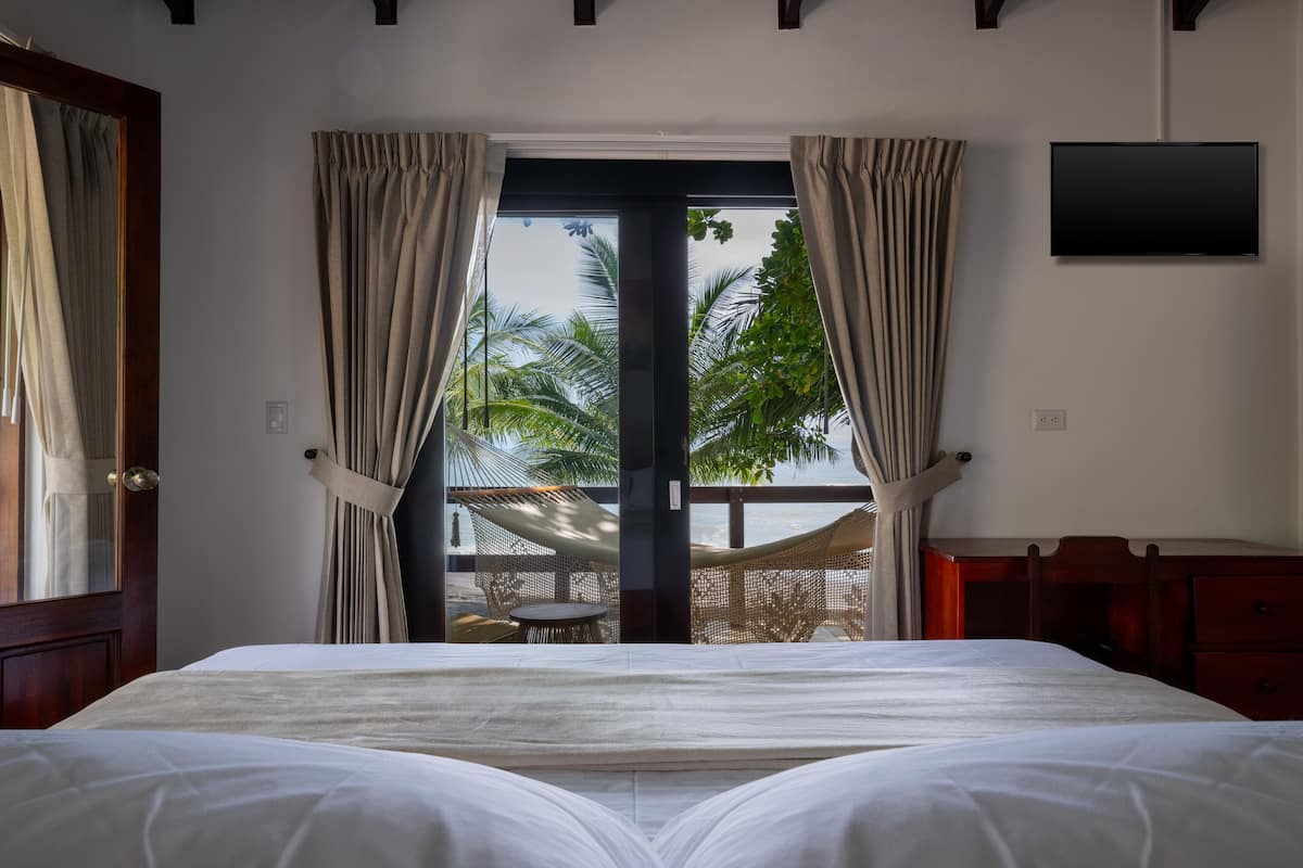 A hotel room with a bed, a TV mounted on the wall, and a view of palm trees through the window.