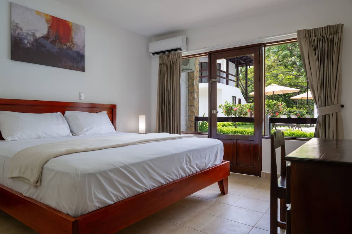 A hotel room with a wooden bed, a desk, and a balcony with outdoor furniture.