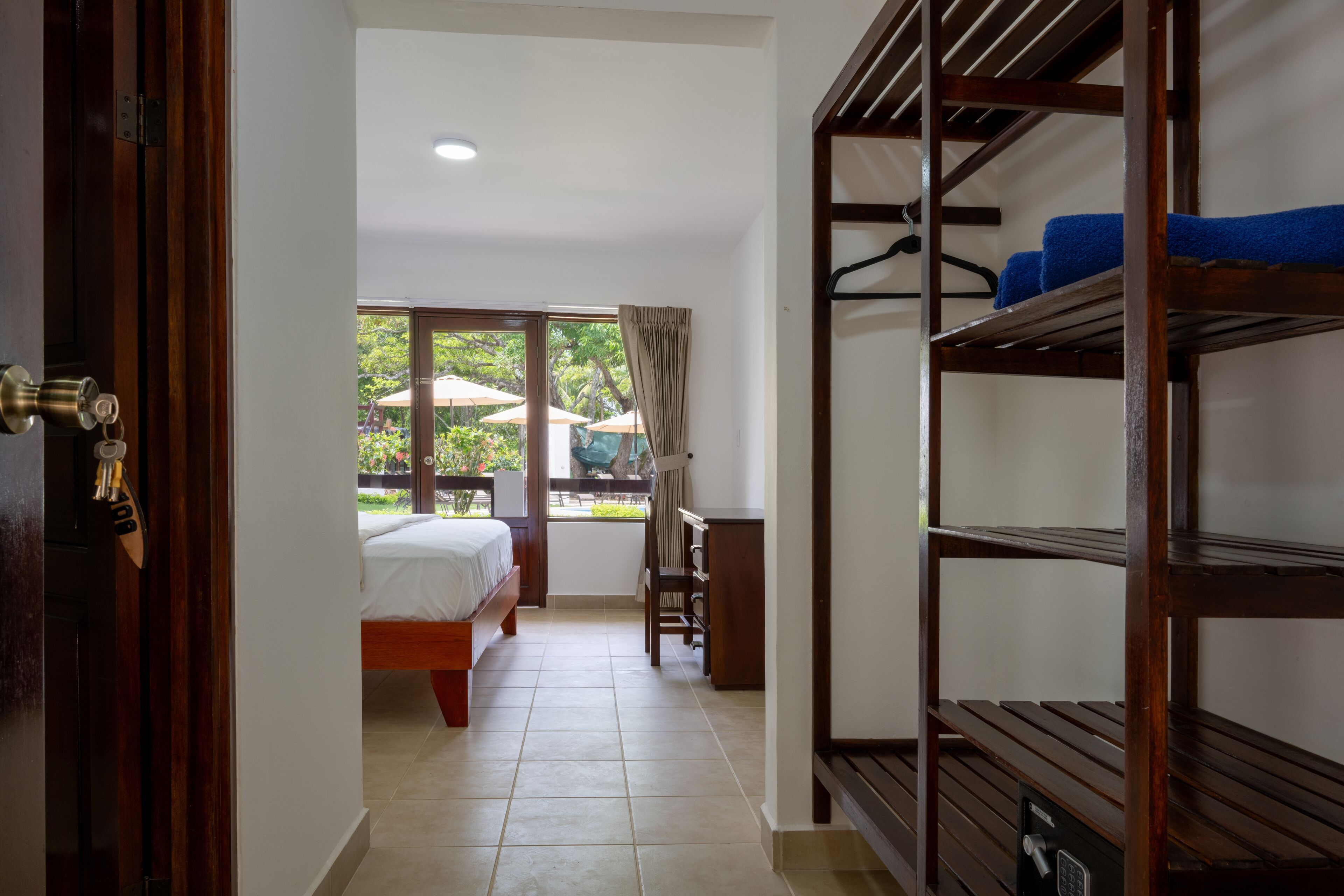 A hotel room with a bed, a desk, a chair, a window with curtains, and a view of the outdoors.
