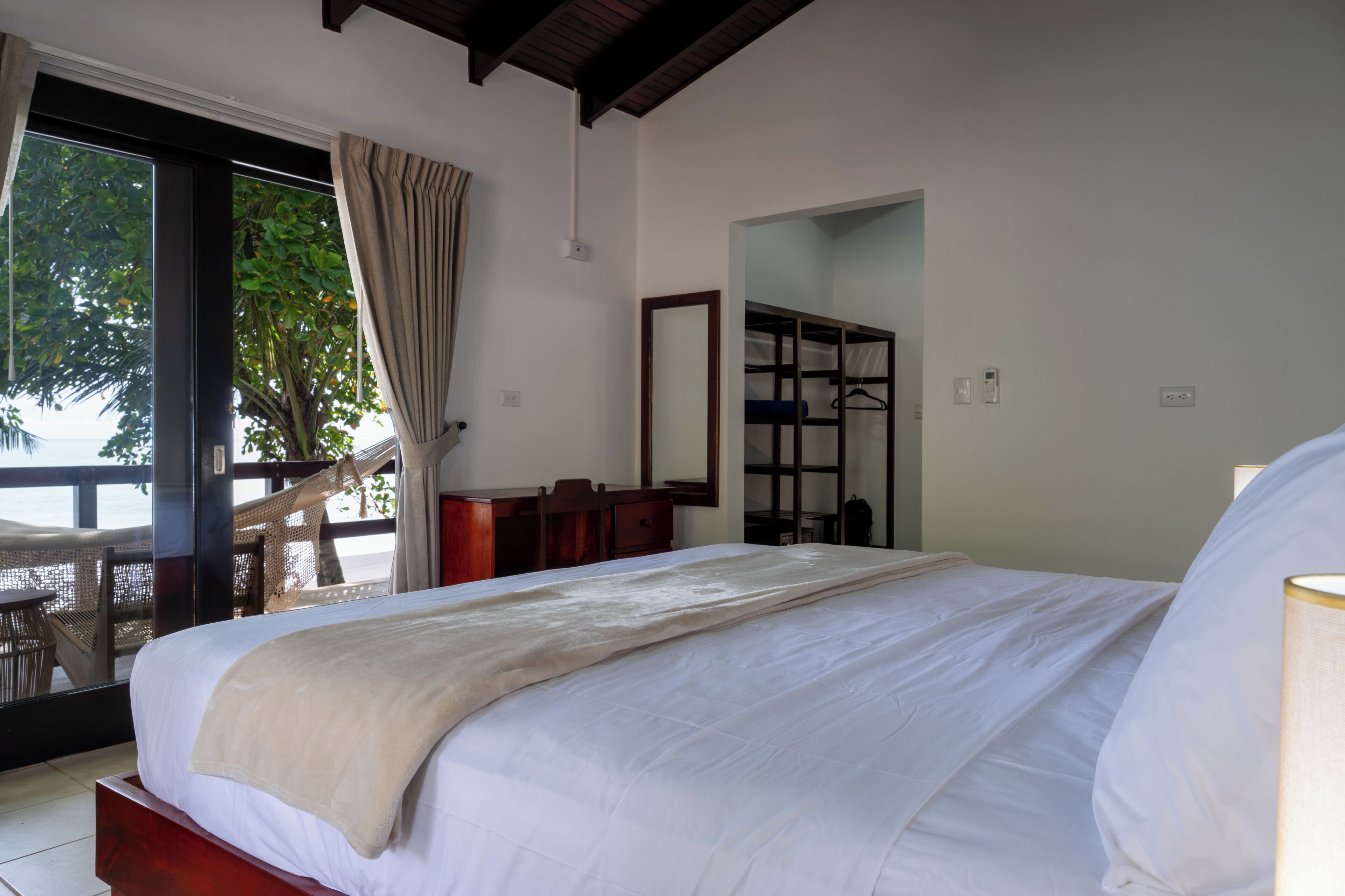 A bedroom with a bed, a wooden dresser, a mirror, and a view of the outdoors.
