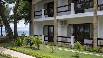 Un edificio de dos pisos con un balcón, rodeado de vegetación tropical y vistas al océano.