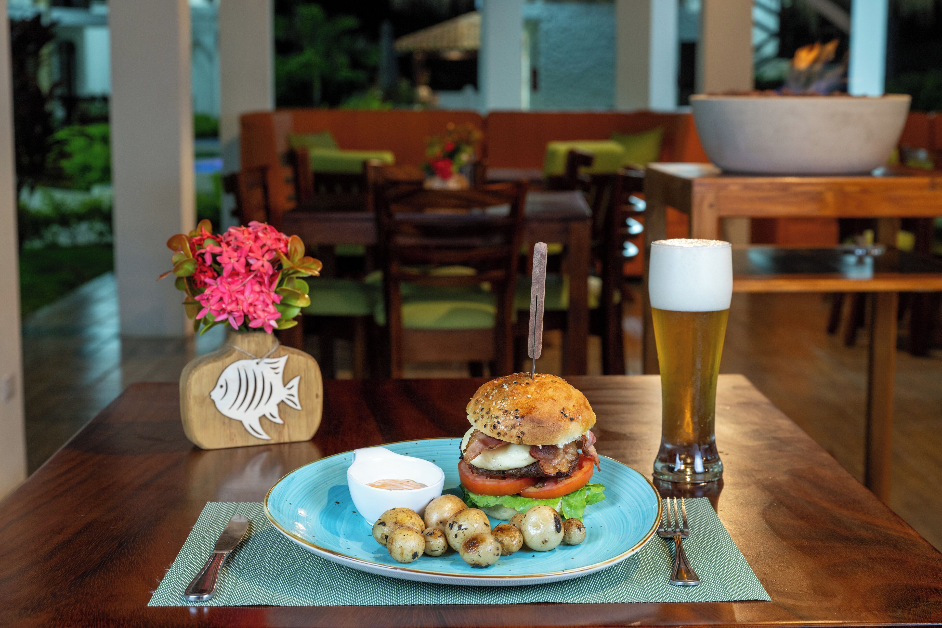 Una mesa de comedor con una hamburguesa, una cerveza en un vaso y un cuenco de salsa.