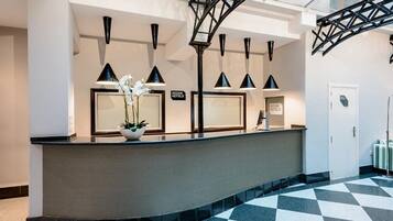 A reception desk with a black and white checkered floor, a potted plant, and a sign reading "ICONIK HOTELS".