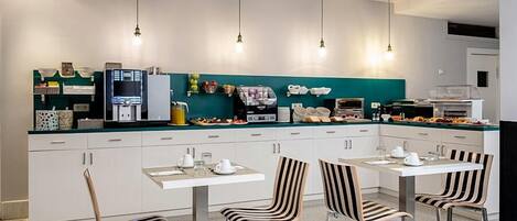 Una cocina moderna con armarios blancos, salpicadero color turquesa y una zona de comedor con sillas a rayas y una mesa blanca.