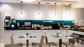 A modern kitchen with white cabinets, a teal accent wall, and a breakfast bar with various food items.