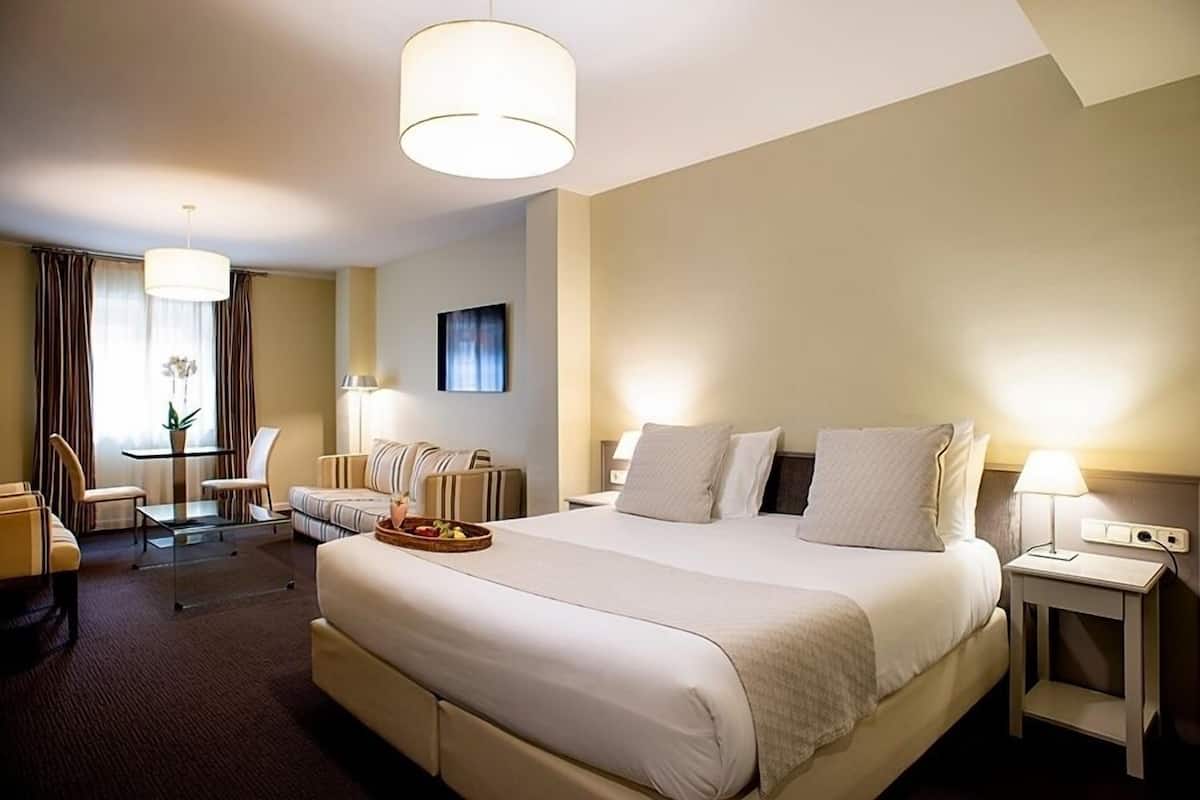Una habitación de hotel con una cama grande, una zona de estar con una mesa y sillas, y dos lámparas de noche.