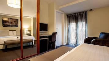 Habitación de hotel con cama, escritorio, silla, televisor y un amplio ventanal con cortinas.