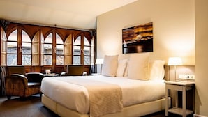 A hotel room with a large bed, a desk with a chair, a small table, and a window with decorative wooden frames. - Ikonik Plaza Mercado (Salamanca)
