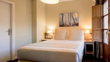 Habitación de hotel con una cama grande, dos lámparas de noche, un cuadro en la pared y un armario de madera.