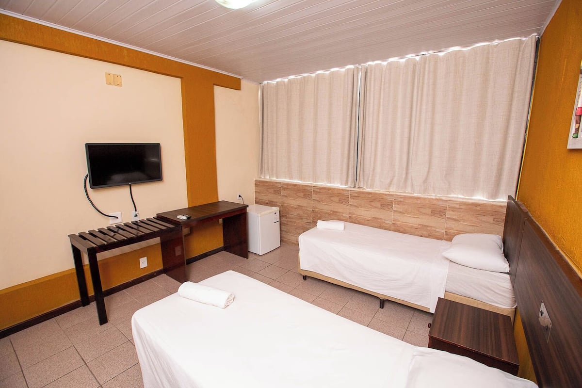 A hotel room with two single beds, a desk with a chair, a television, and a window with curtains.