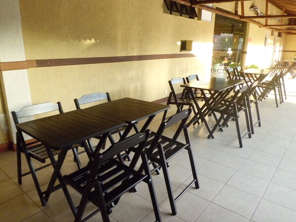 A dining area with multiple tables and chairs, a tiled floor, and a plain wall with a window.