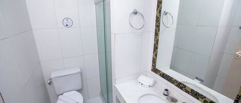 Un baño pequeño y limpio con inodoro, lavamanos y cabina de ducha de vidrio.