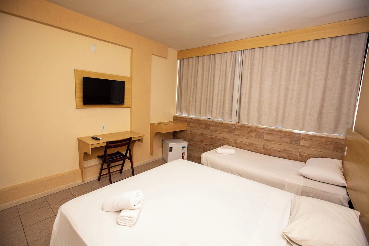 A hotel room with two beds, a desk, a chair, a TV, and a window with curtains.