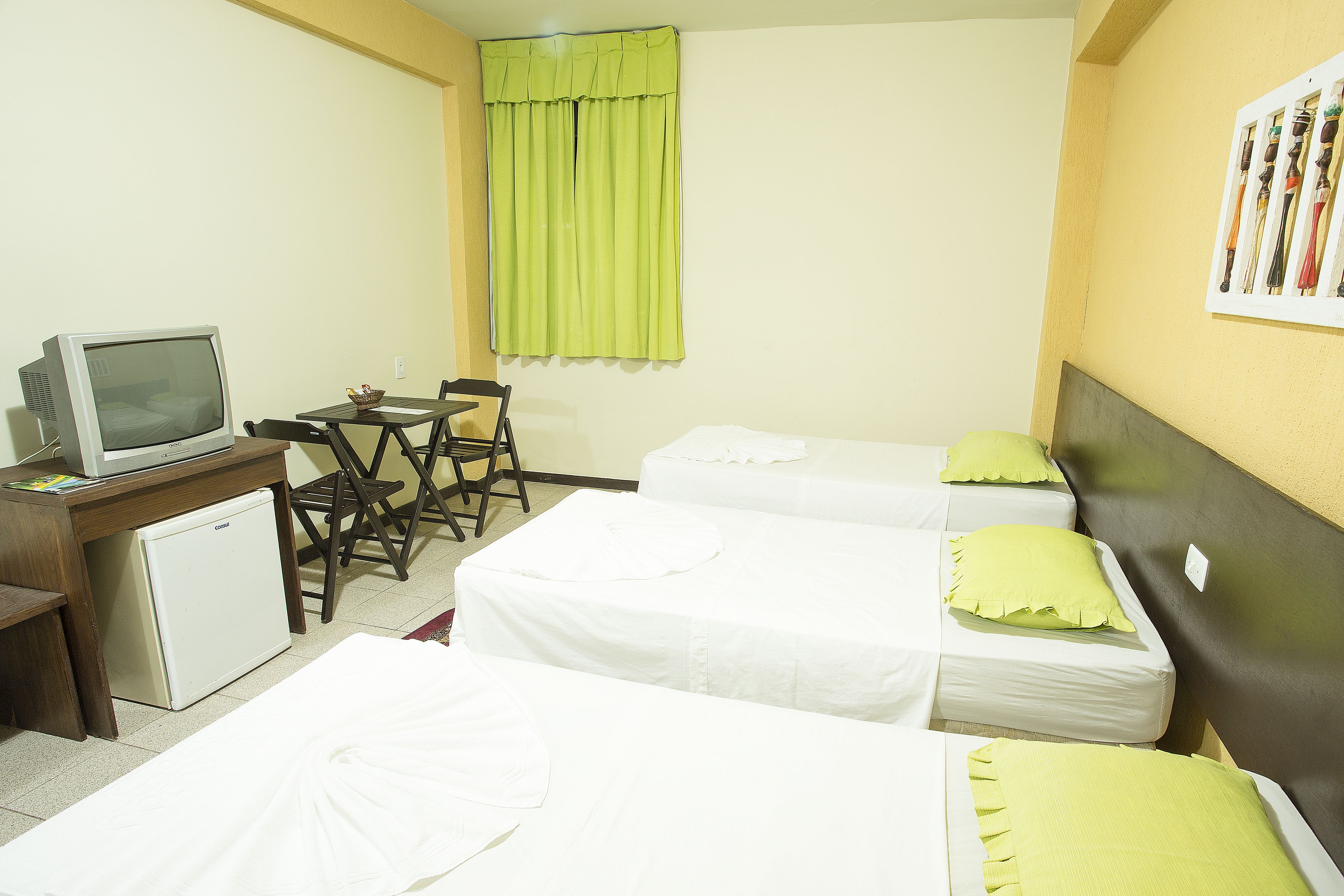 A hotel room with two beds, a desk with a television, and a small refrigerator.