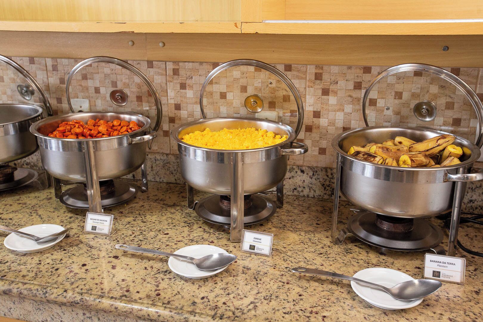 Buffet-style food stations with various dishes like carrots, yellow rice, and plantains.