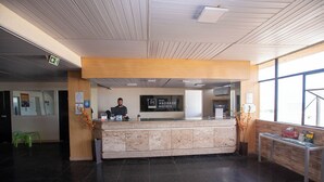 Mostrador de recepción de hotel con recepcionista, pantalla digital y vista a la ventana.