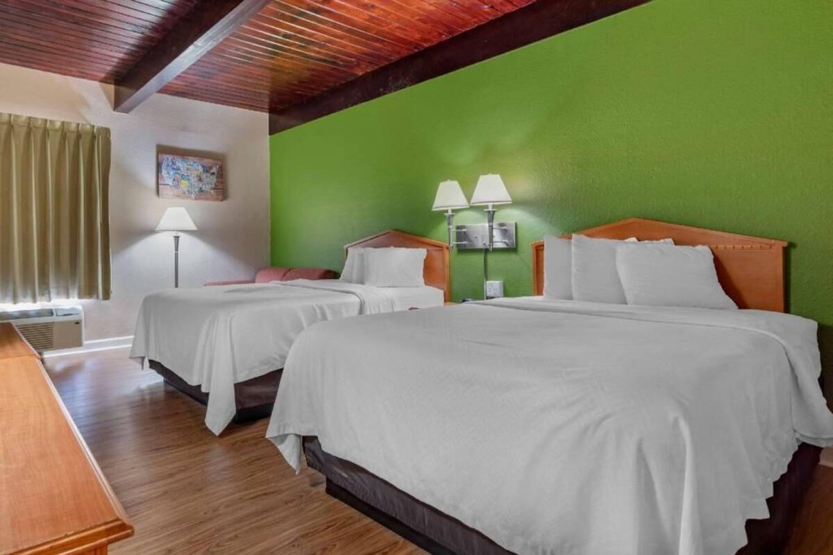 A hotel room with two beds, a wooden desk, a green wall, and a ceiling with exposed beams.