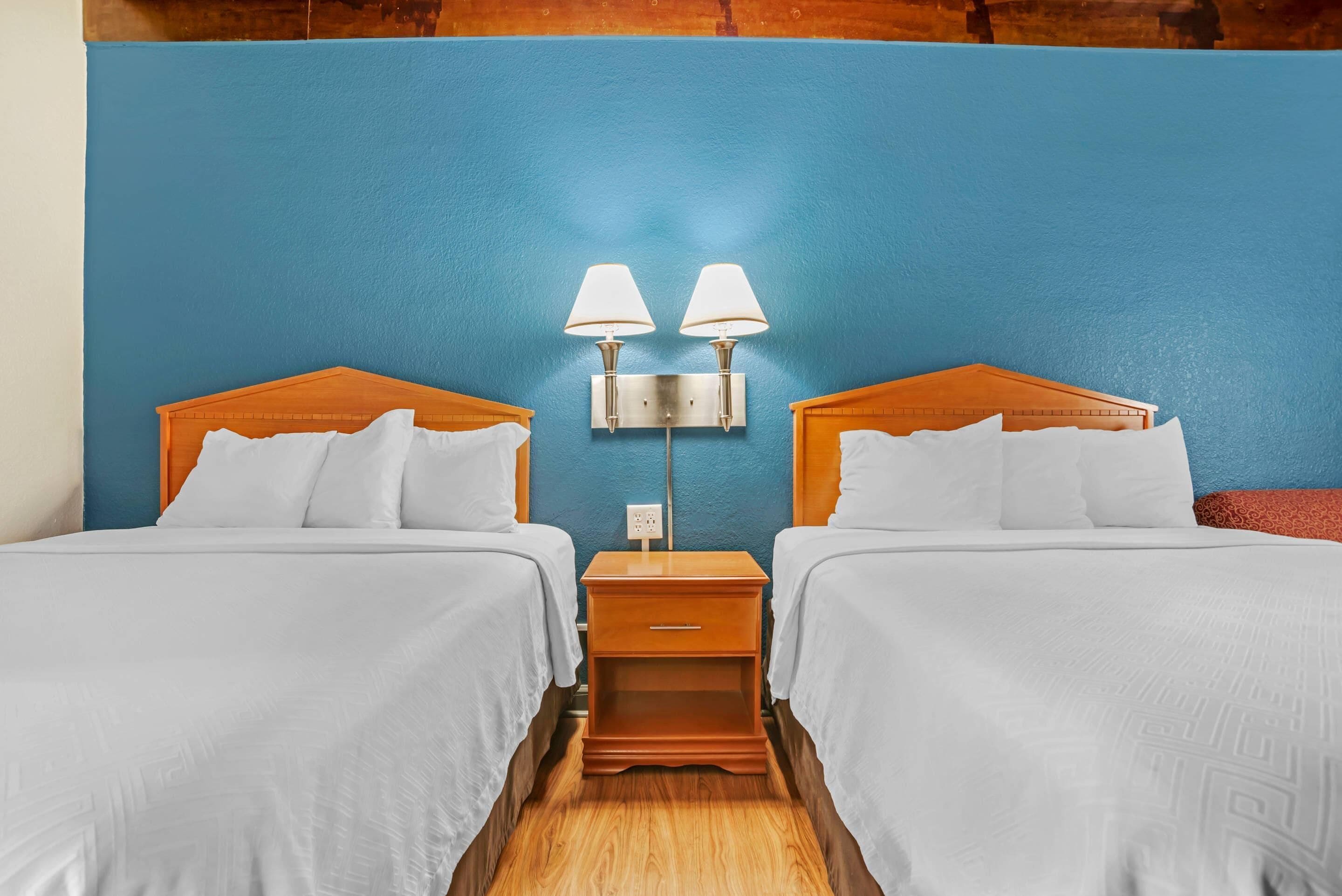 Ein Hotelzimmer mit zwei Betten, einem Nachttisch mit Lampen und einer blauen Akzentwand.