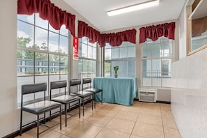 Une pièce avec de grandes fenêtres, une table recouverte d’une nappe bleue et quatre chaises.