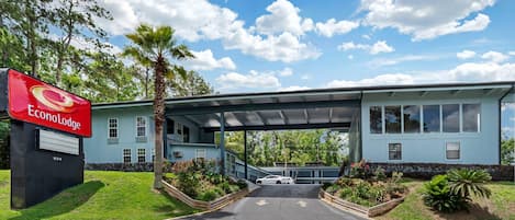 A hotel entrance with a covered walkway, a signboard, and a parking area.