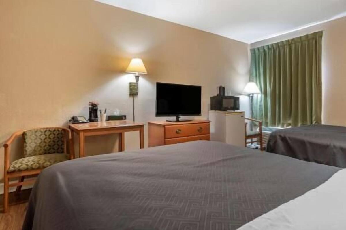 Une chambre d’hôtel avec un lit, un bureau avec une télévision, une chaise et une fenêtre avec des rideaux.