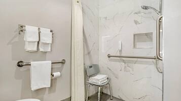 A bathroom with a shower, a toilet, a grab bar, a chair, and towels.