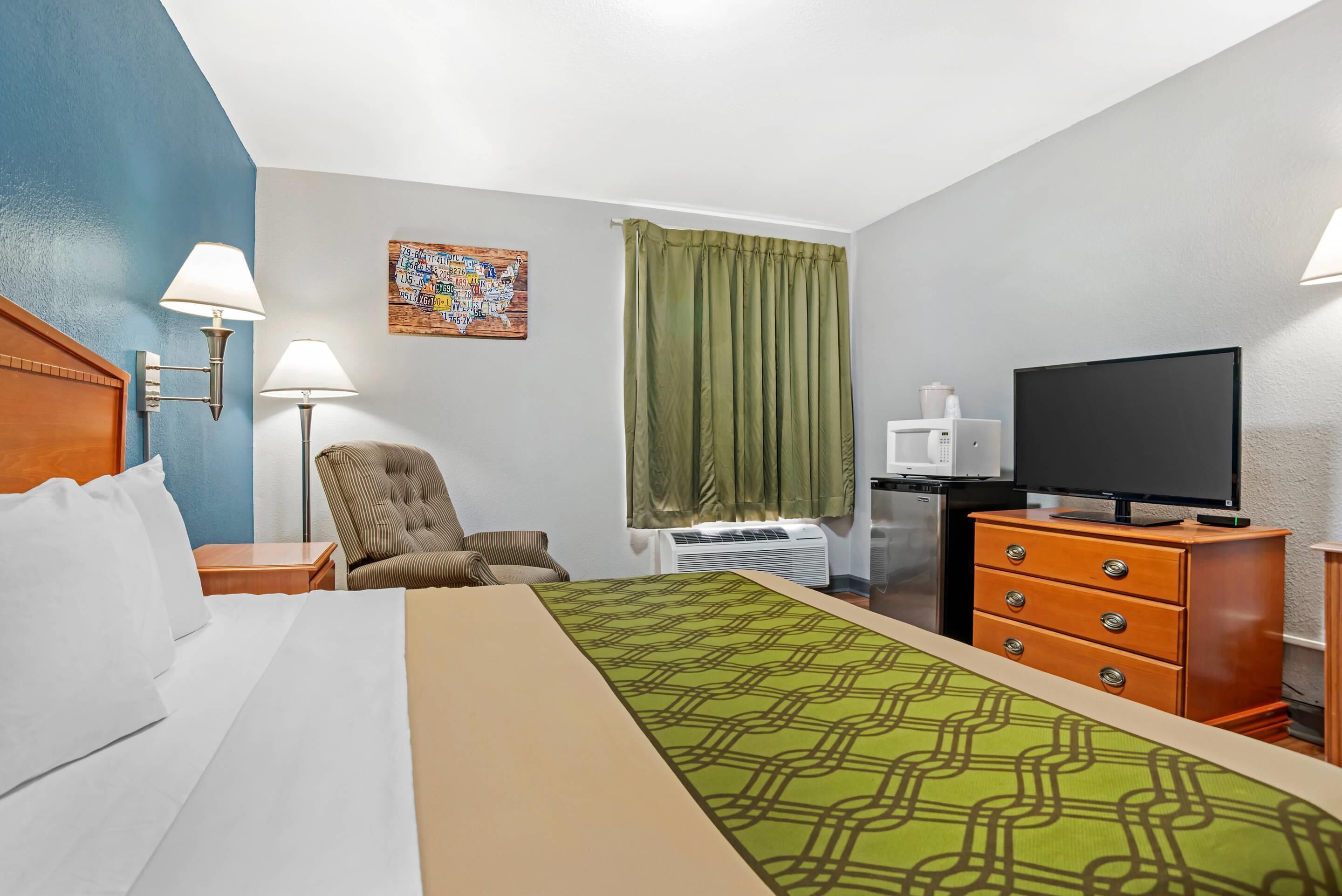 A hotel room with a bed, a chair, a desk with a television, and a window with curtains.