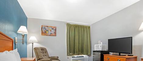 A hotel room with a bed, a chair, a desk with a television, and a window with curtains.