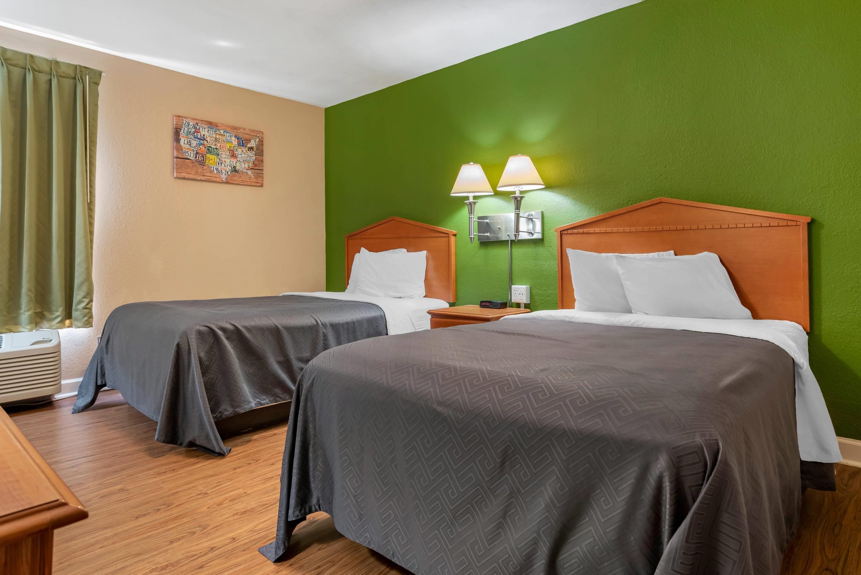 Hotellihuone, jossa on kaksi sänkyä, vihreä seinä, puulattia ja taulu seinällä.