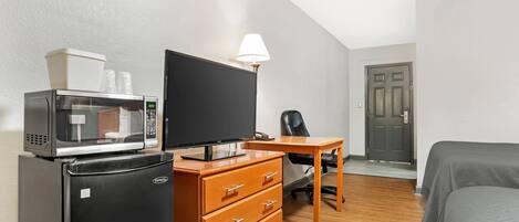 A compact hotel room with a kitchenette, a flat-screen TV, a wooden desk, a chair, and a bed.