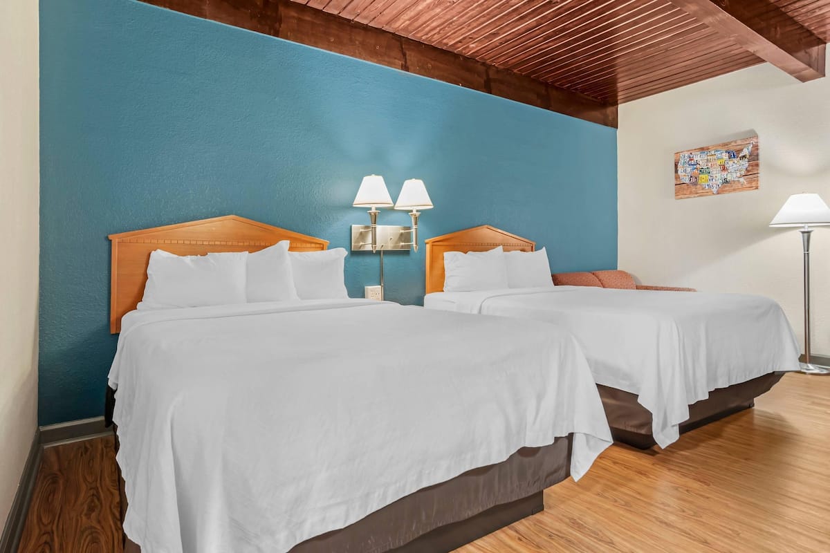 A hotel room with two beds, wooden headboards, a blue accent wall, and a map artwork.