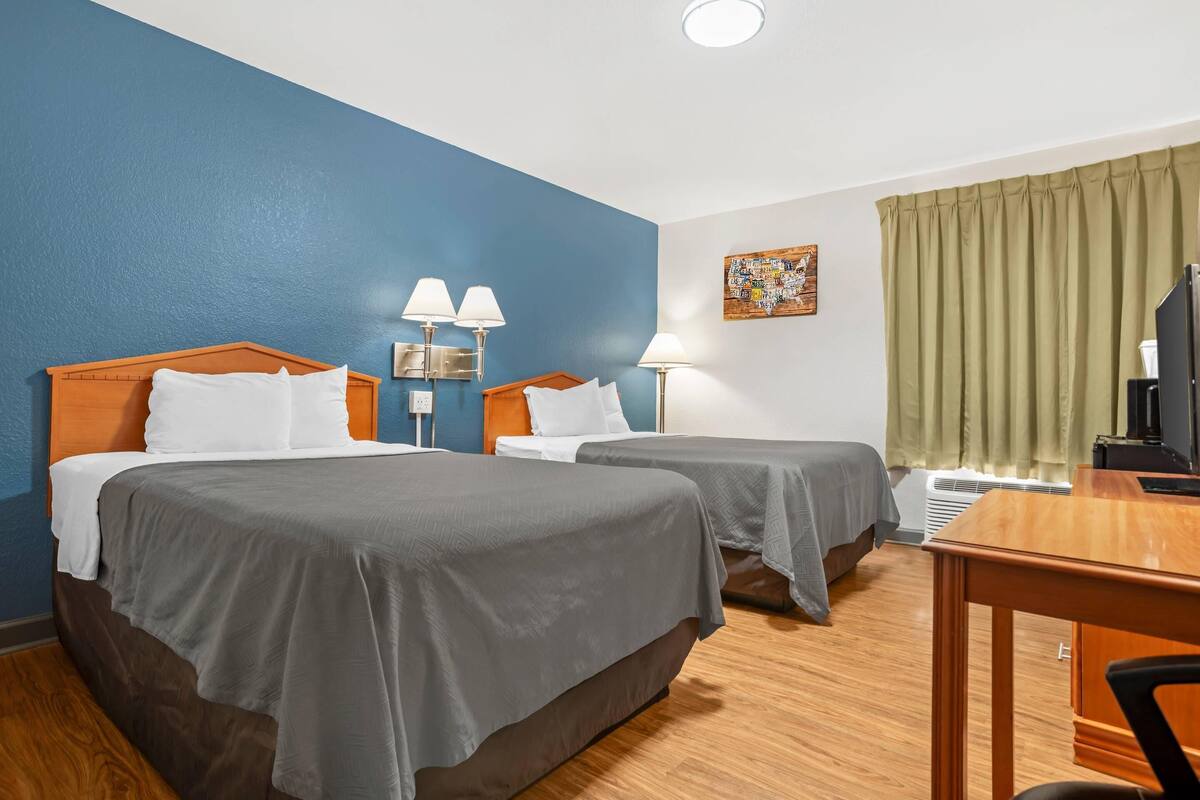 A hotel room with two beds, a desk, a chair, a TV, and a painting on the wall.