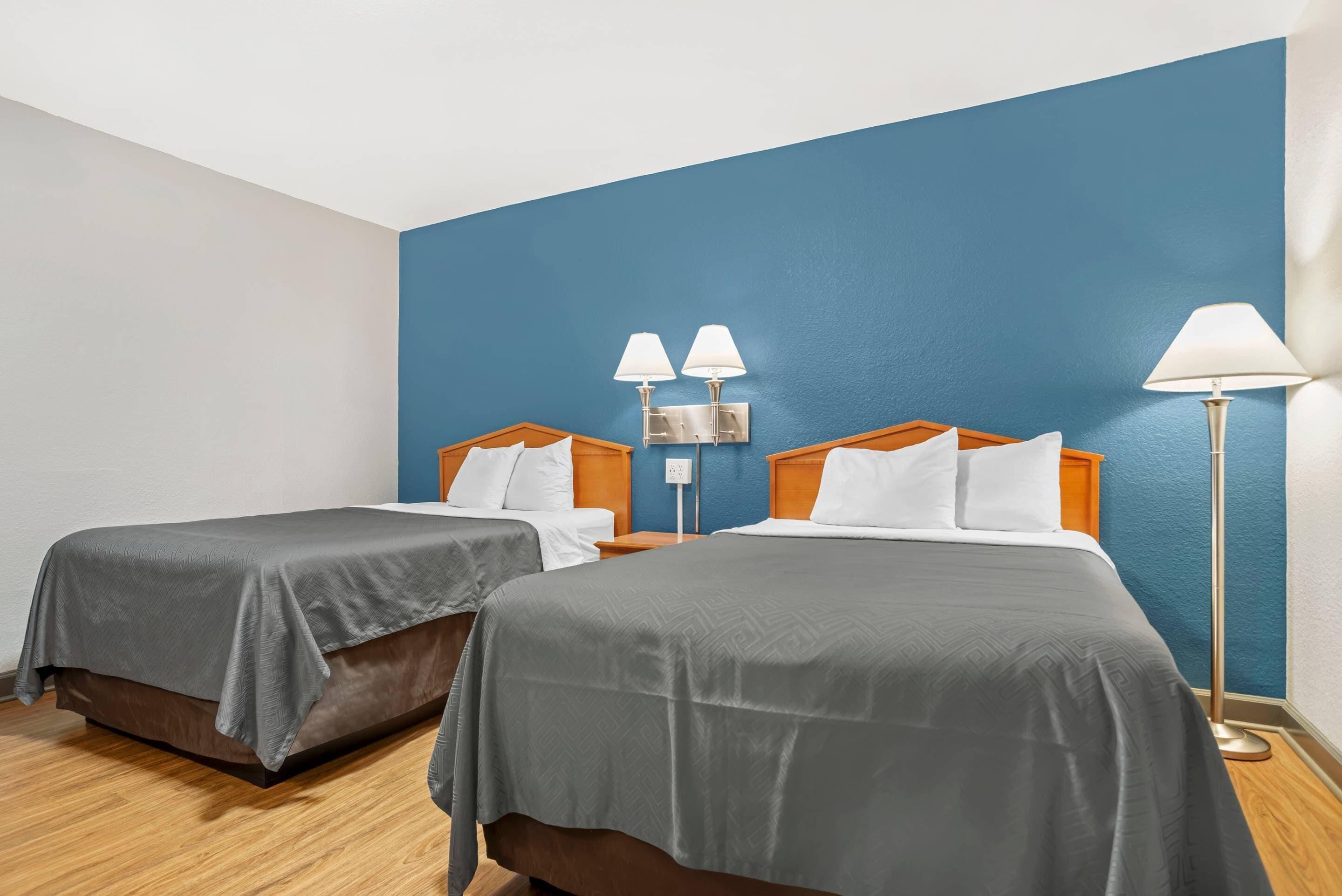 Habitación de hotel con dos camas, una pared de acento azul y una lámpara de pie.