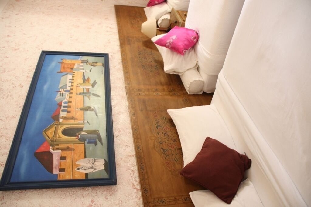 Une œuvre d’art encadrée posée sur le sol, un canapé blanc avec des coussins roses et bruns, et un plancher en bois.