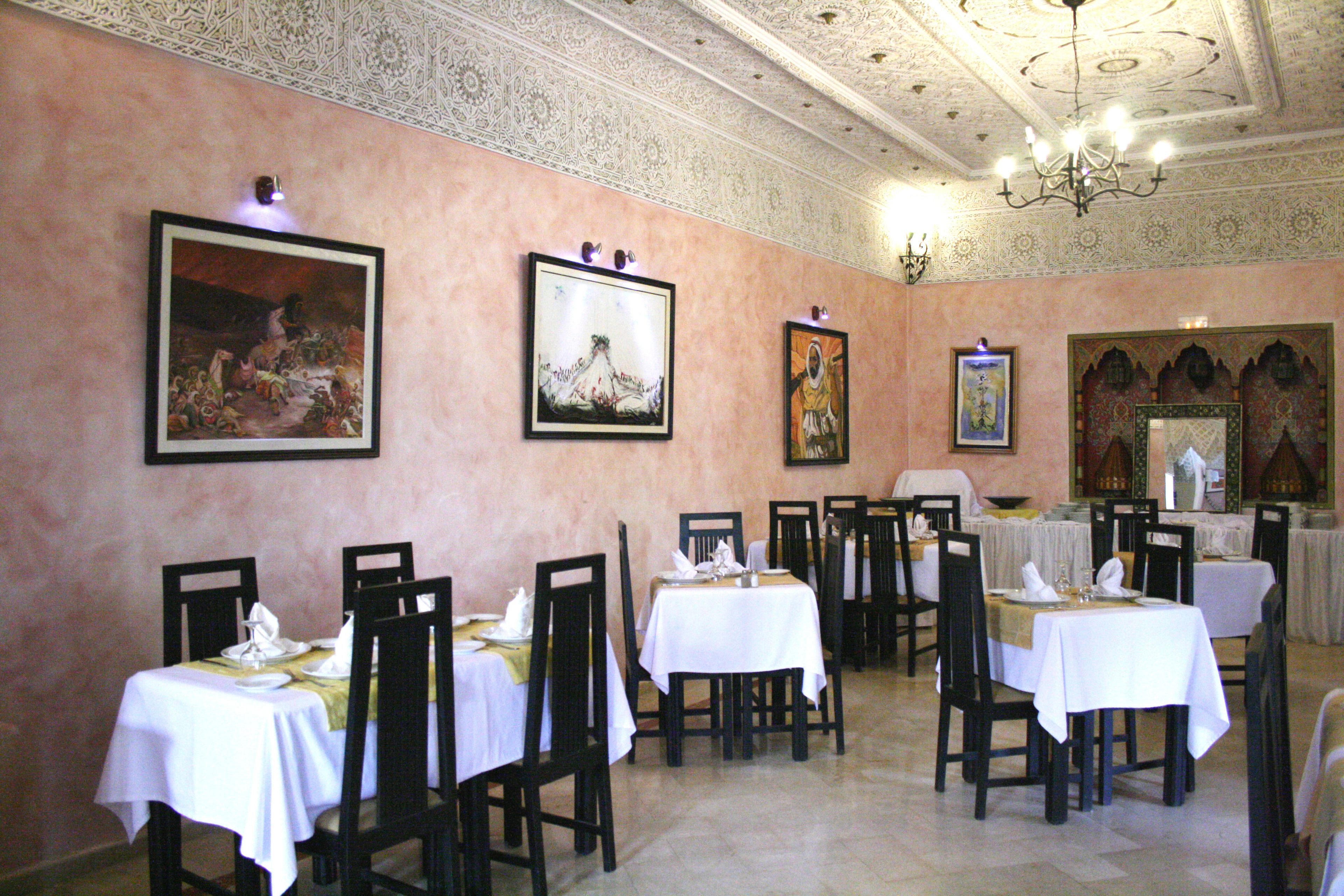 A dining area with tables set for service, framed artwork on the walls, and a chandelier.