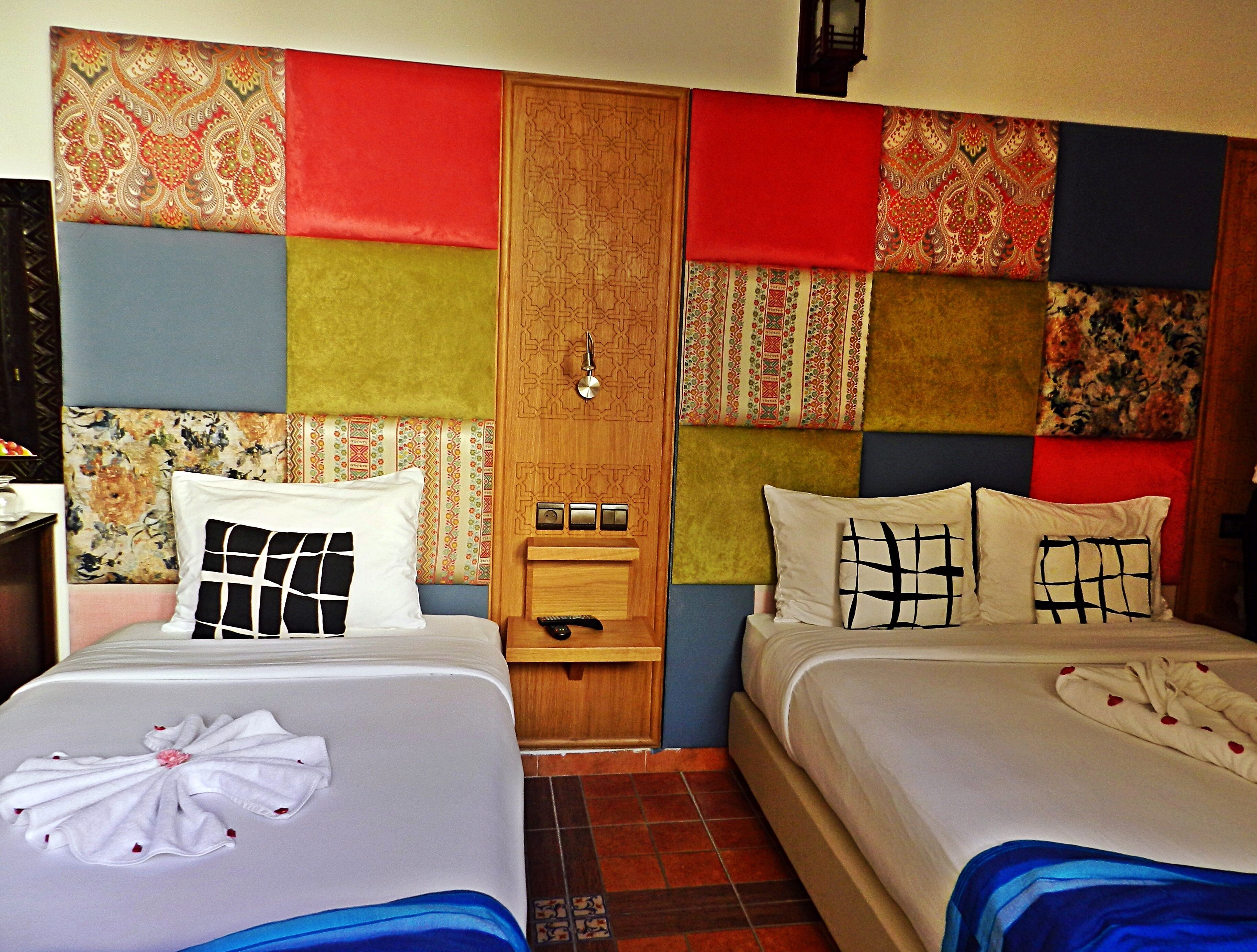 A hotel room with two beds, a wooden wardrobe, and a small bedside table with a remote control.